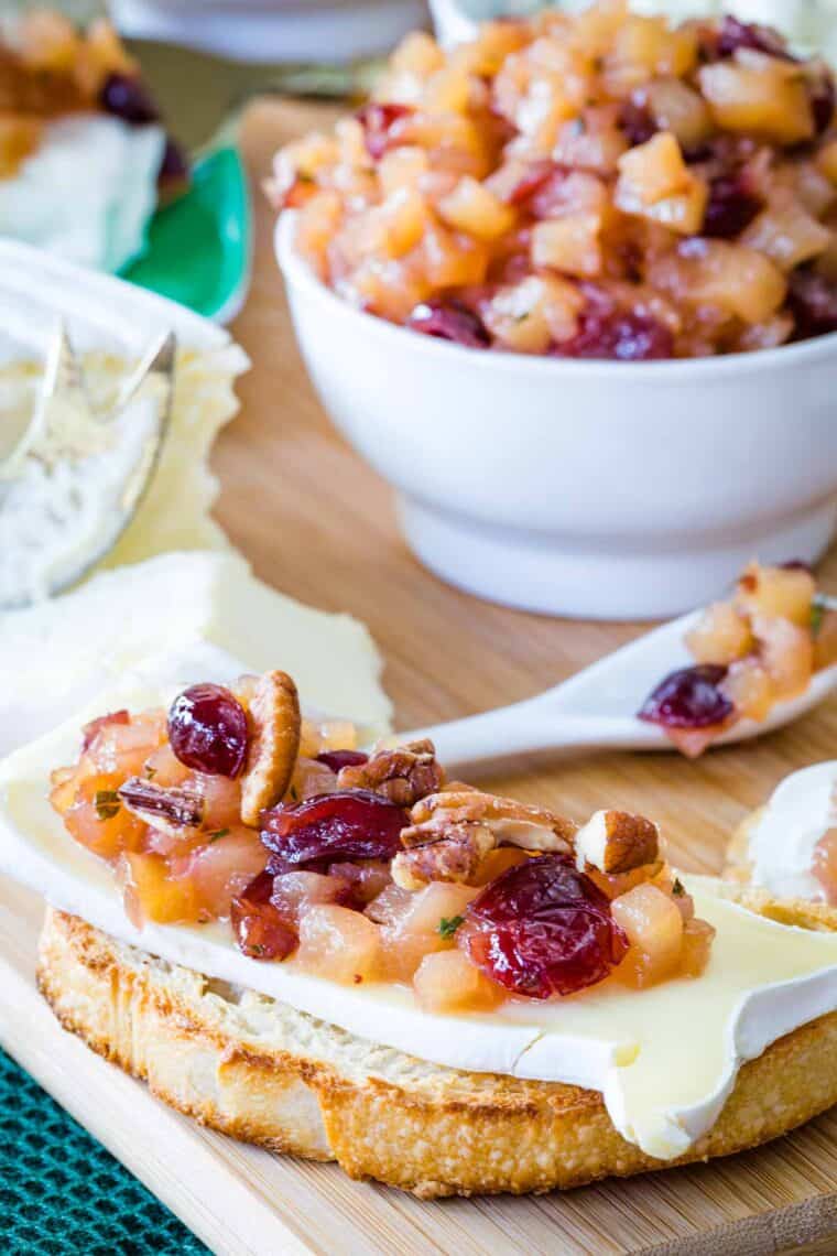 A slice of toasted baguette topped with brie cheese, chutney, and chopped pecans.