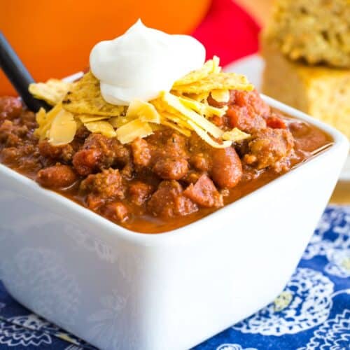 a bowl of the world's best chili with shredded cheese, crushed tortilla chips, and sour cream on top.
