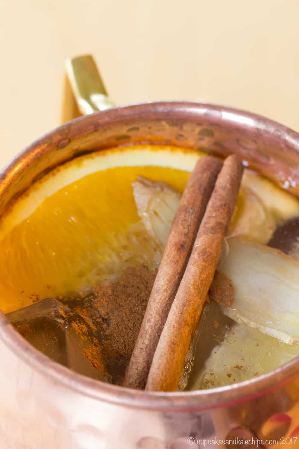 Closeup of the cinnamon stick, fresh ginger, and orange slice garnishes on top of a cocktail in a copper mug.