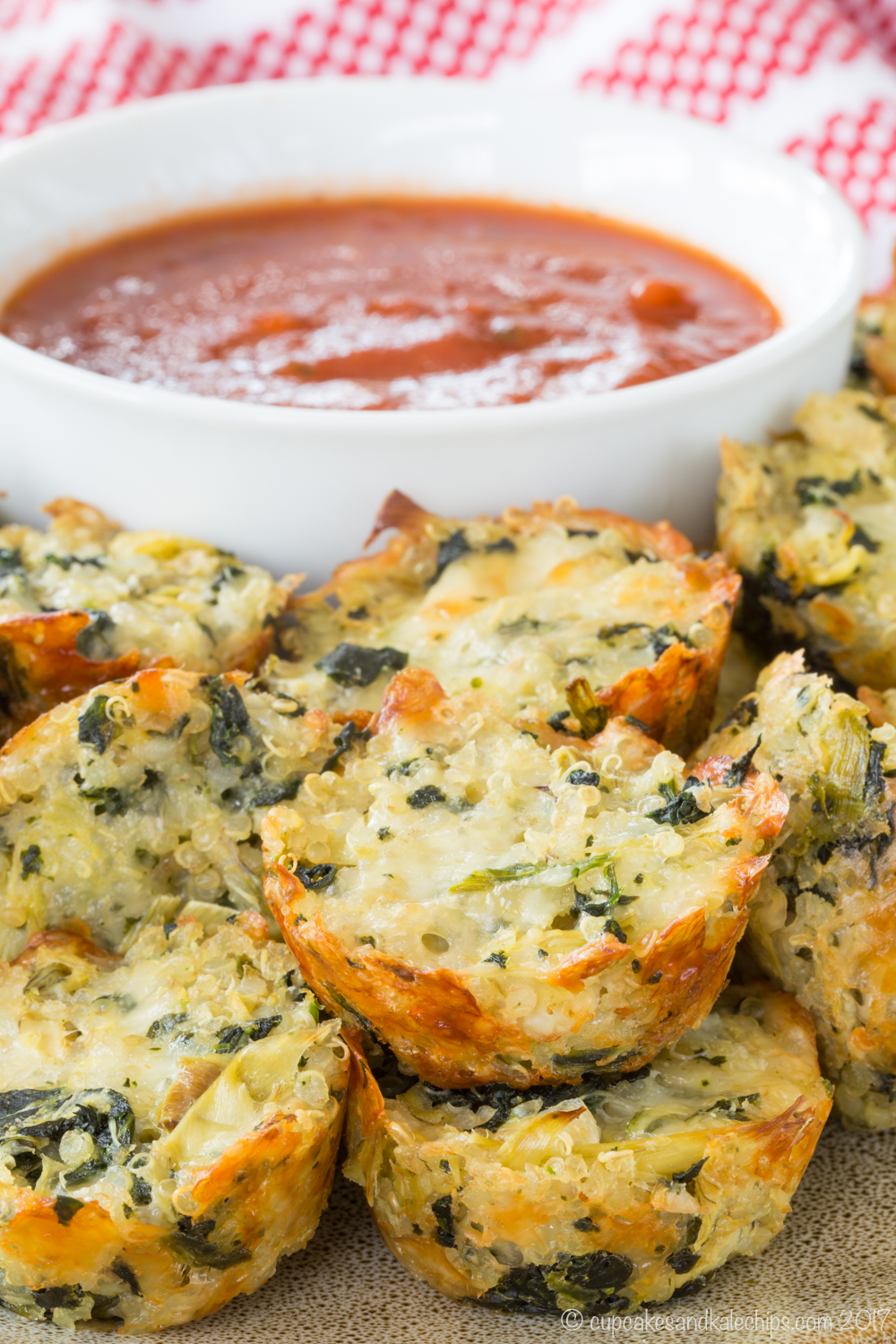 Closeup of Spinach Artichoke Quinoa Bites with a bowl of marinara sauce behind them.