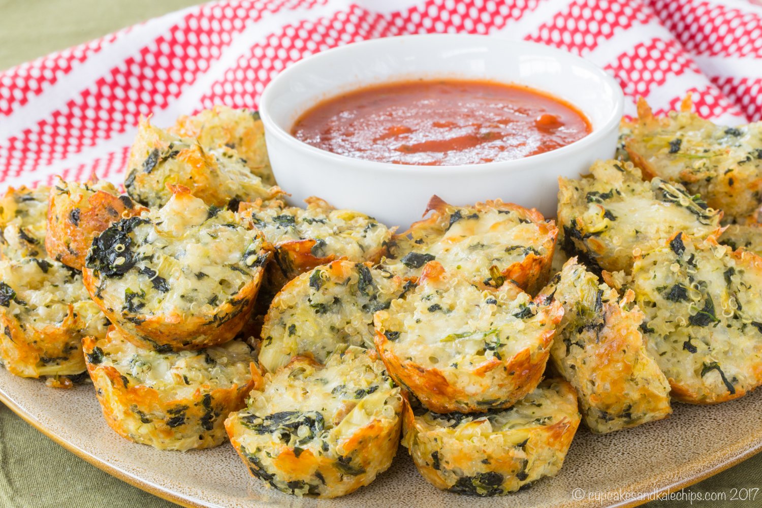 A platter of mini-muffin sized quinoa bites surrounding a bowl of tomato sauce.