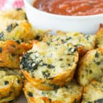 Spinach Artichoke Quinoa Bites piled around a bowl of tomato sauce.