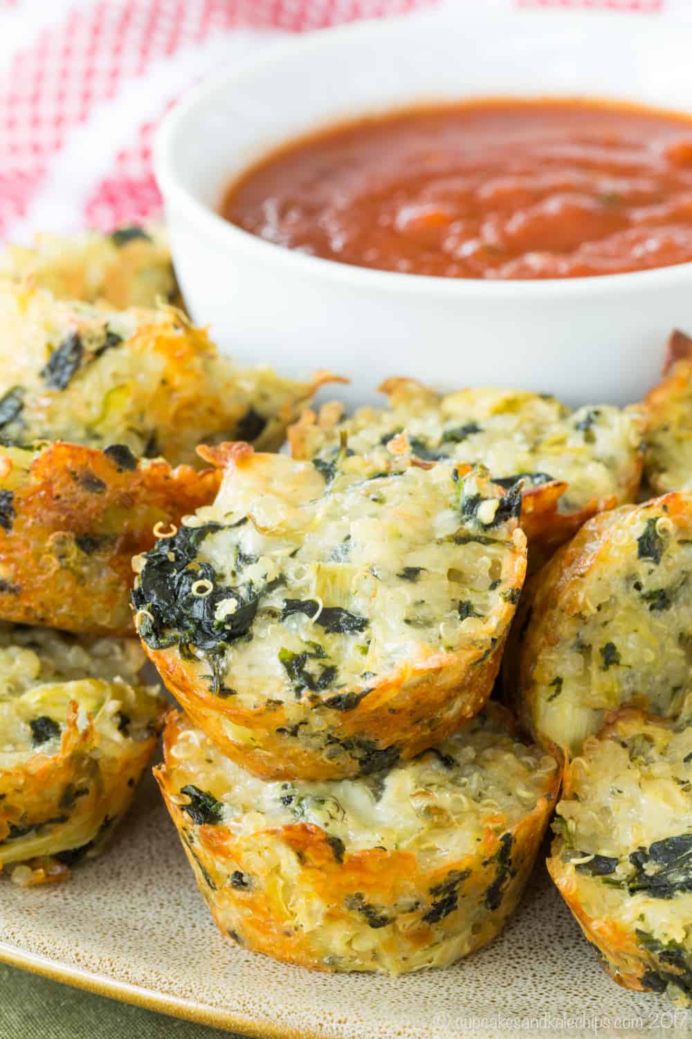 Spinach Artichoke Quinoa Bites piled around a bowl of tomato sauce.