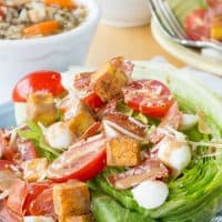 A wedge salad made with Romaine salad topped with fresh mozzarella, tomatoes, and crispy prosciutto.