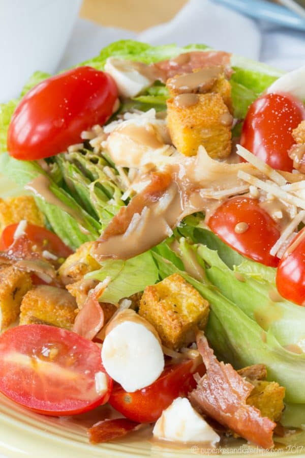 Closeup of tomatoes, prosciutto, fresh mozzarella, and creamy balsamic dressing on a romaine wedge salad