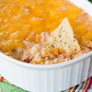 hot shrimp jambalaya dip in a white casserole dish with a tortilla chip stuck in it.