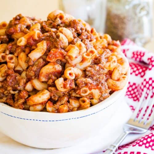 A bowl overfilled with beefaroni made of elbow macaroni coated in meat sauce.