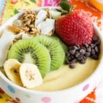 pink and white polka dot bowl filled with a thick pale yellow smoothie and fruit and granola on top