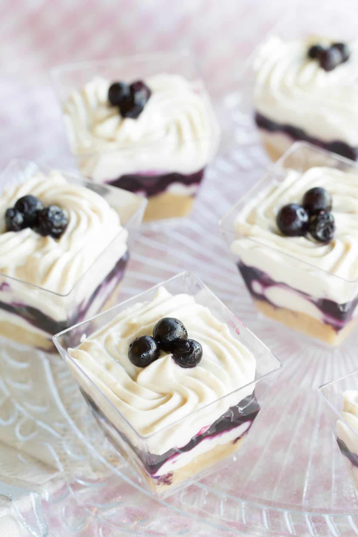 Looking down on a platter of mini dessert parfaits topped with small wild blueberries.