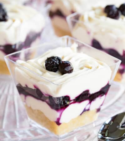 One blueberry cheesecake cup with a spoon next to it and a few more blurred in the background.