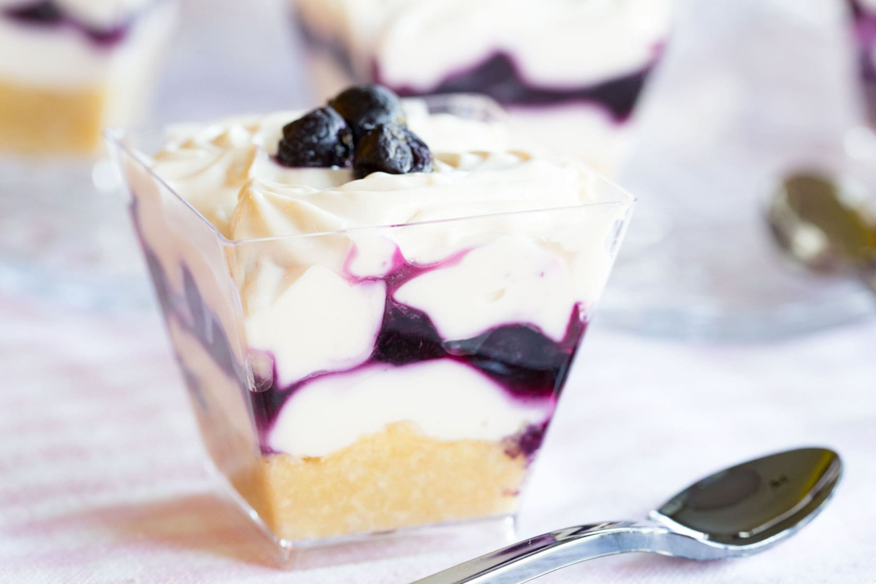 A mini blueberry cheesecake parfait with a small spoon next to it.