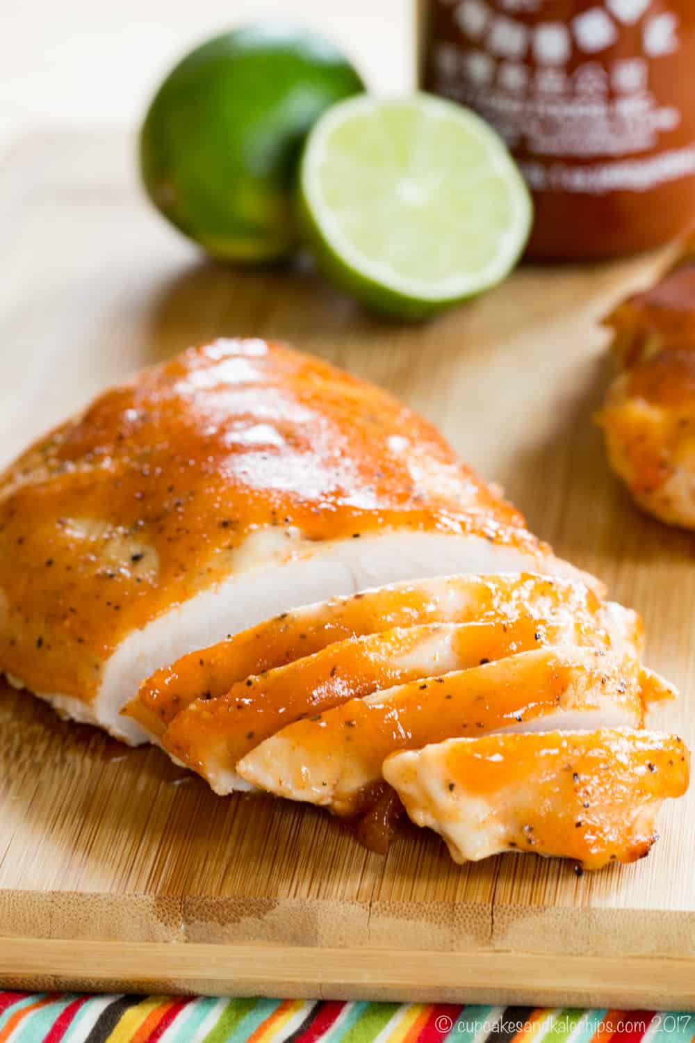 A sliced turkey breast tenderloin coated in glaze on a cutting board with limes and a bottle of sriracha sauce in the background.