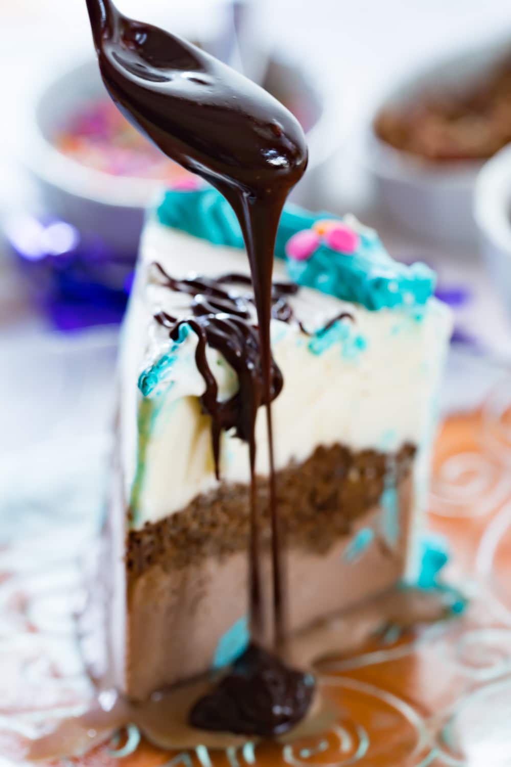 Chocolate glaze being drizzled off a spoon over a piece of ice cream cake.