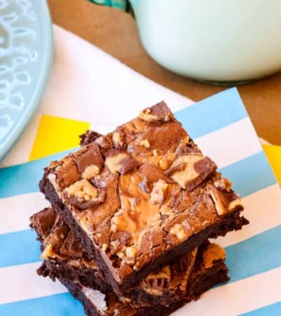 Three stacked Peanut Butter Cup Brownies on a blue and white striped napkin with a glass of milk.