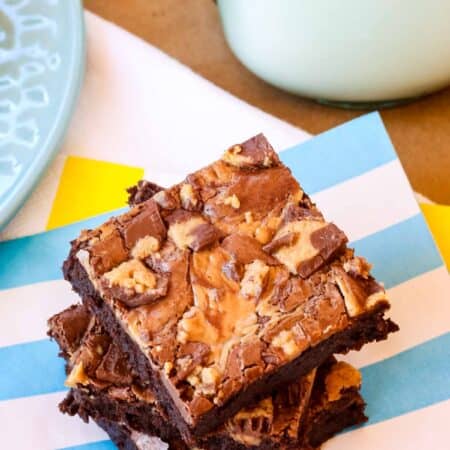 Three stacked Peanut Butter Cup Brownies on a blue and white striped napkin with a glass of milk.