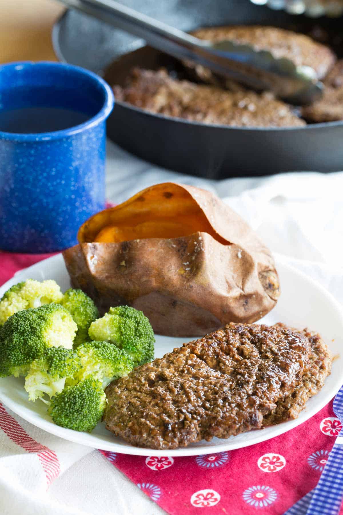 A plated dinner of cube steak, a baked sweet potato, and steamed broccoli.