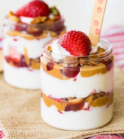 Two peanut butter and jelly yogurt parfaits in jars with a polka dot spoon in the one in front.