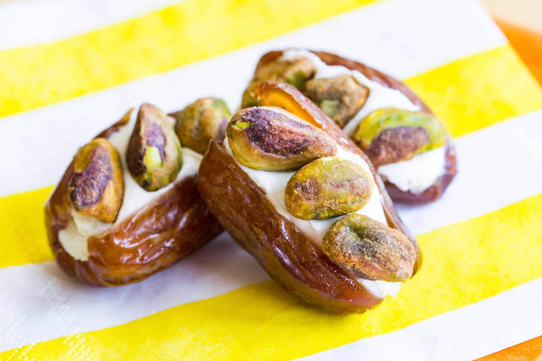A few dates stuffed with cream cheese and three pistachios each on a yellow and white striped napkin.