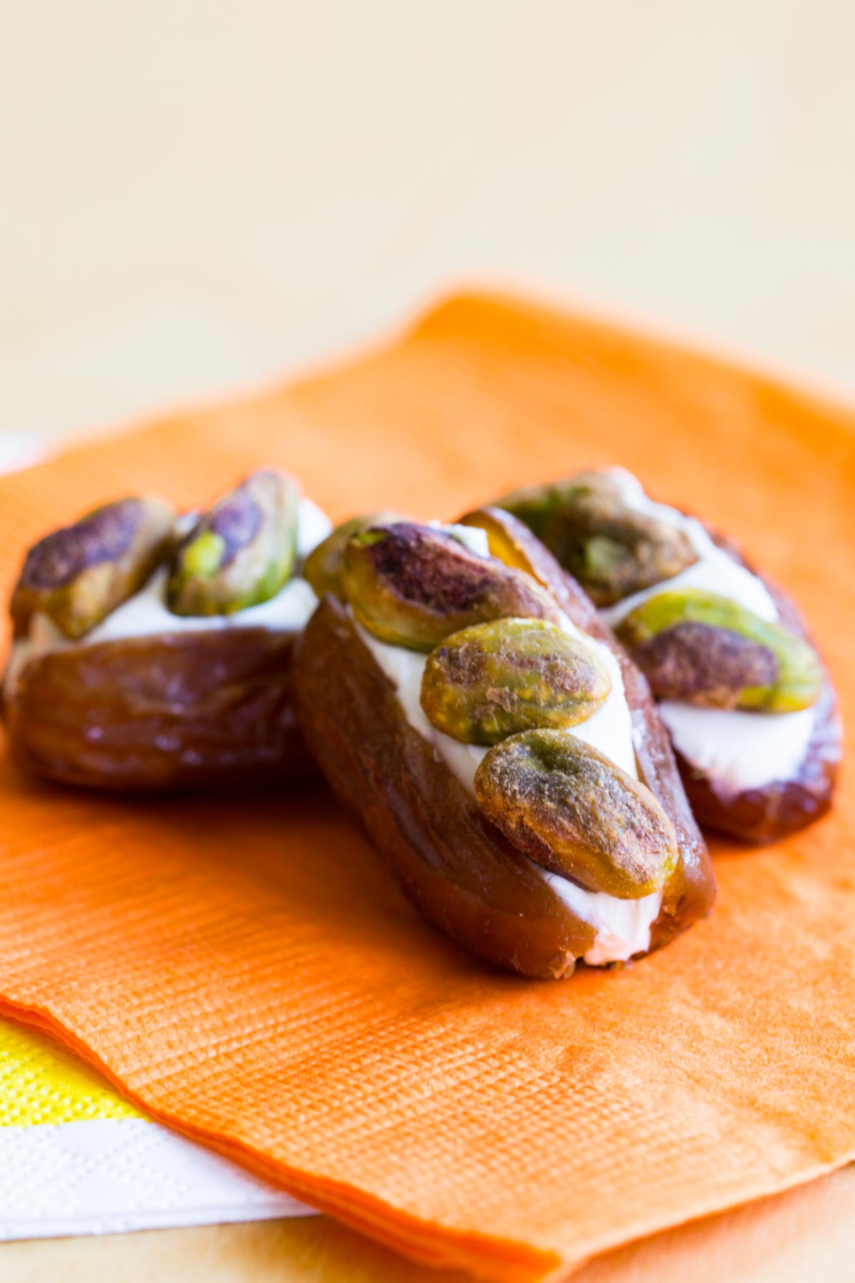 Three Pistachio Cream Cheese Stuffed Dates on an orange paper napkin.