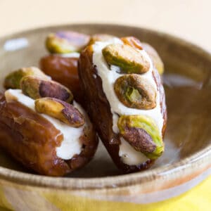 A small green dish of cream cheese stuffed dates with pistachios pressed into them.