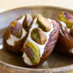 A miniature bowl with three dates stuffed with cream cheese and three pistachios in each of them.
