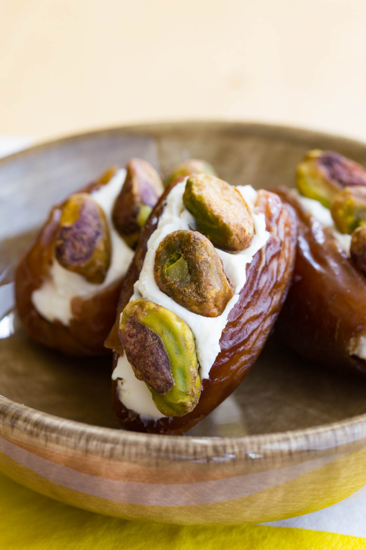 A miniature bowl with three dates stuffed with cream cheese and three pistachios in each of them.