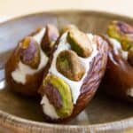 Three cream cheese stuffed dates studded with pistachios in a small bowl with text overlay on the image.
