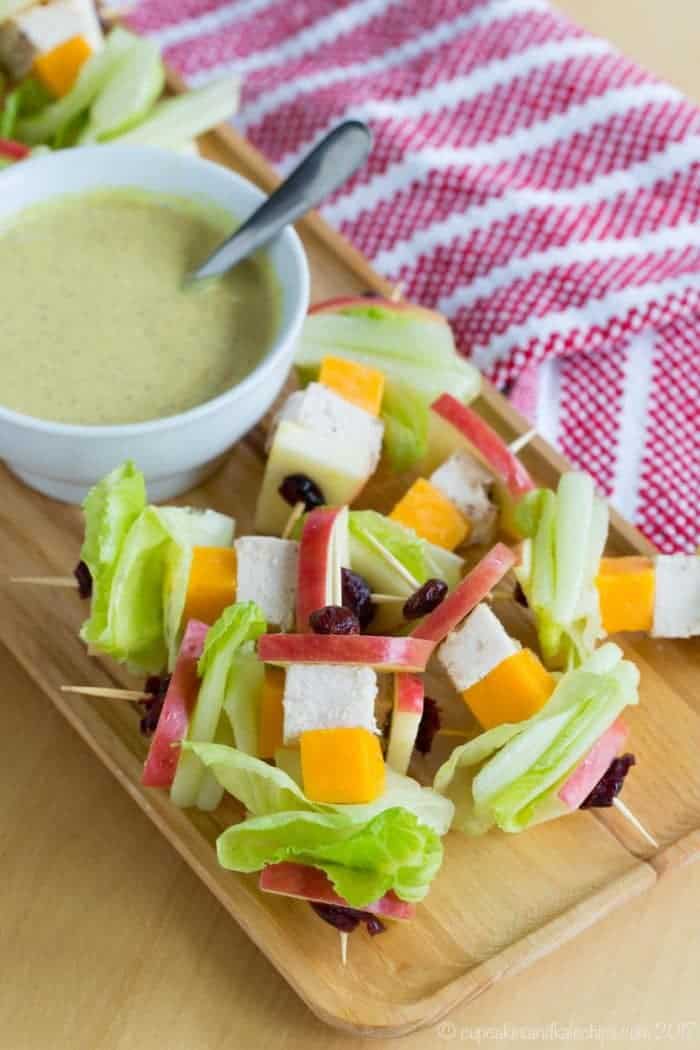 A wodden platter with Apple Chicken Salad Skewers and honey mustard dressing