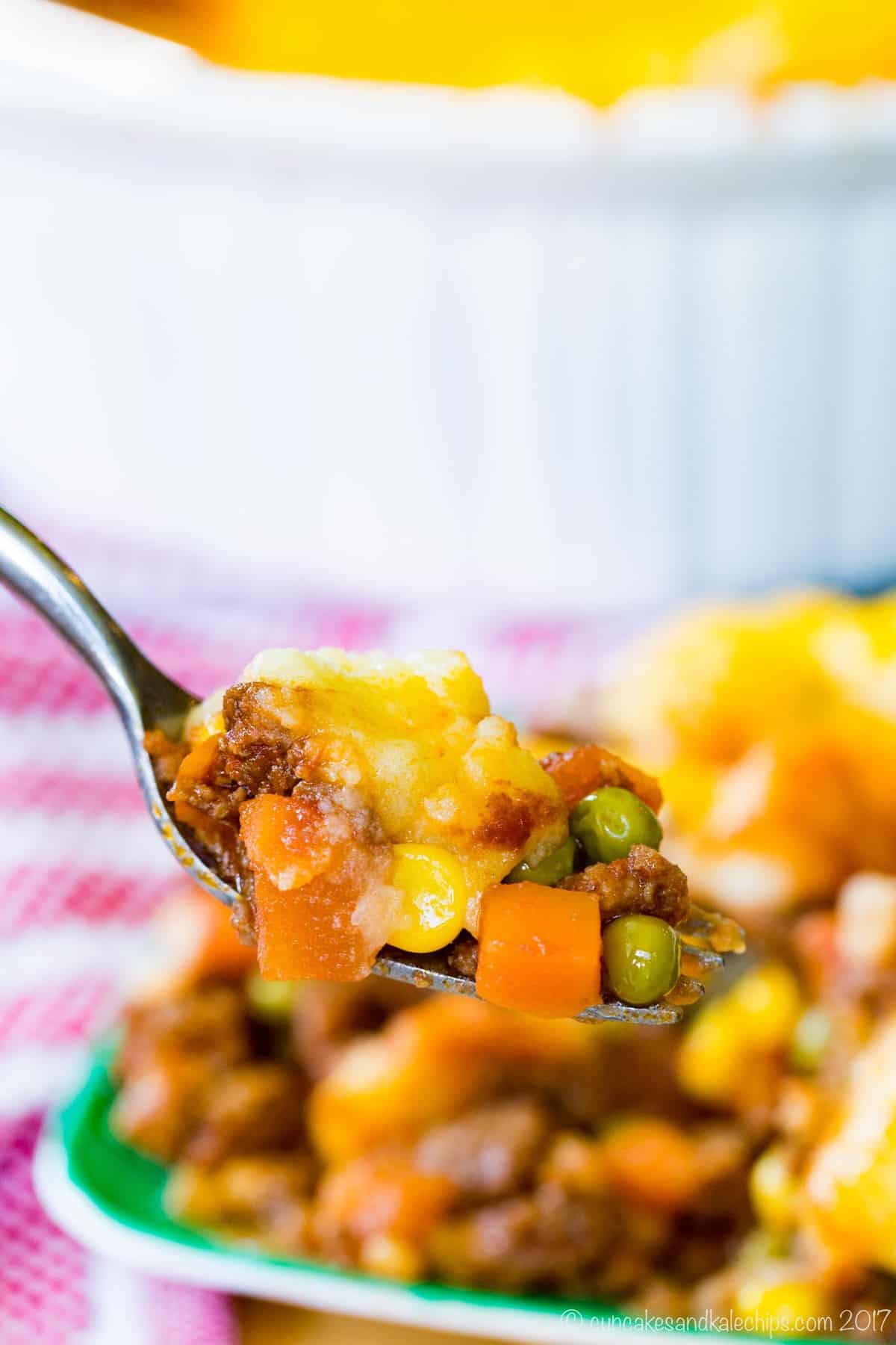 a bite of shepherds pie on a fork with bits of ground beef, corn, peas, and carrots