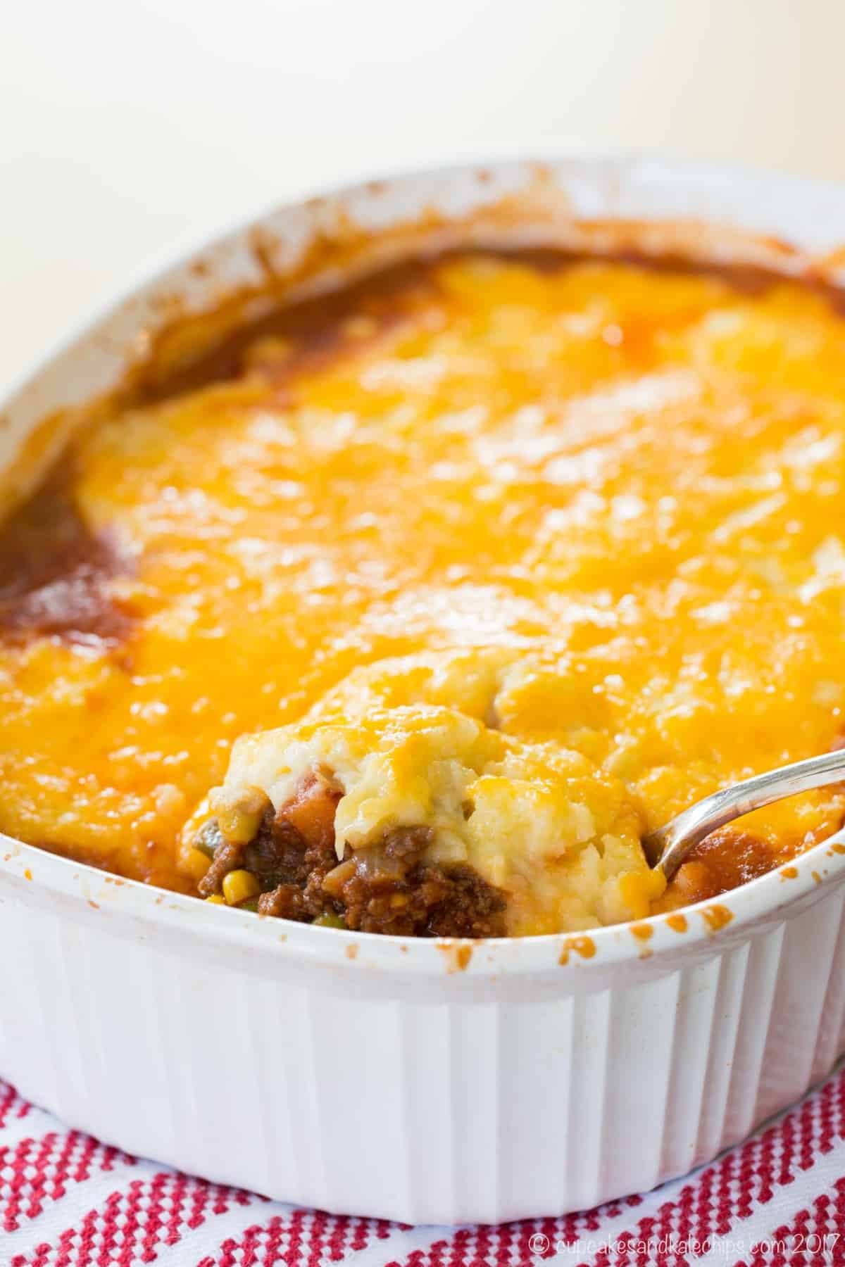 serving spoon just starting to pick up a bit of the shepherd's pie to the edge of the casserole dish