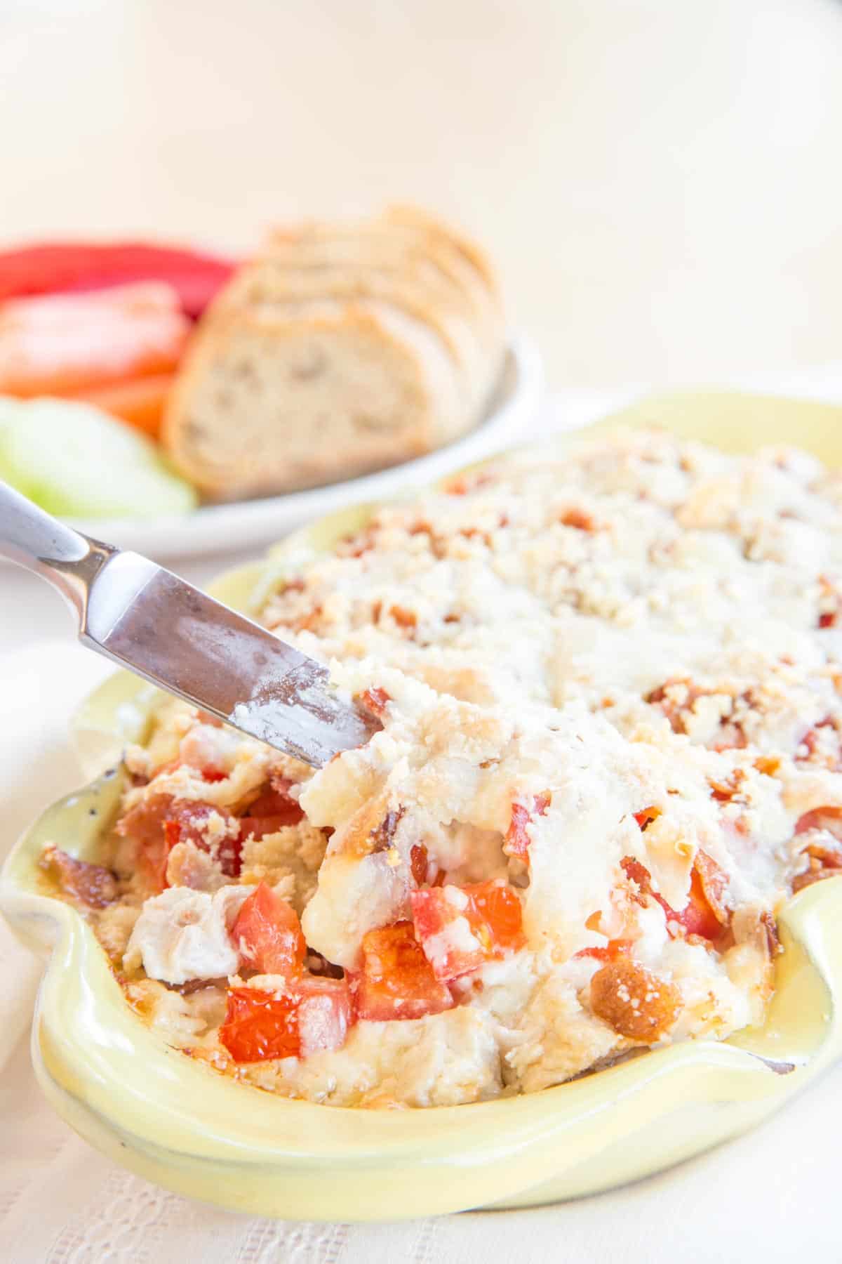 Hot cheesy dip filled with turkey, bacon, and tomatoes in a yellow casserole dish