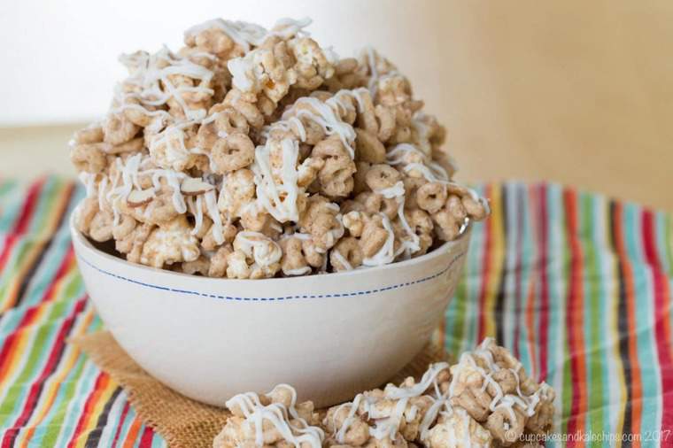 A bowl of gluten-free popcorn snack mix filled with cheerios, topped with a creamy white chocolate drizzle.