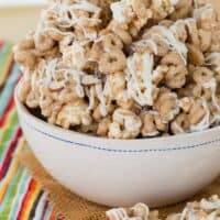 A bowl of gluten-free popcorn snack mix filled with cheerios, topped with a creamy white chocolate drizzle.