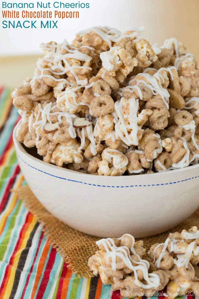 A bowl of gluten-free popcorn snack mix filled with cheerios, topped with a creamy white chocolate drizzle.