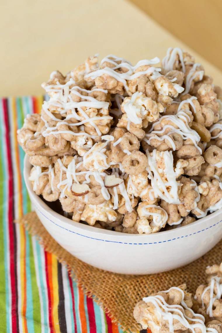 A bowl of gluten-free popcorn snack mix filled with cheerios, topped with a creamy white chocolate drizzle.