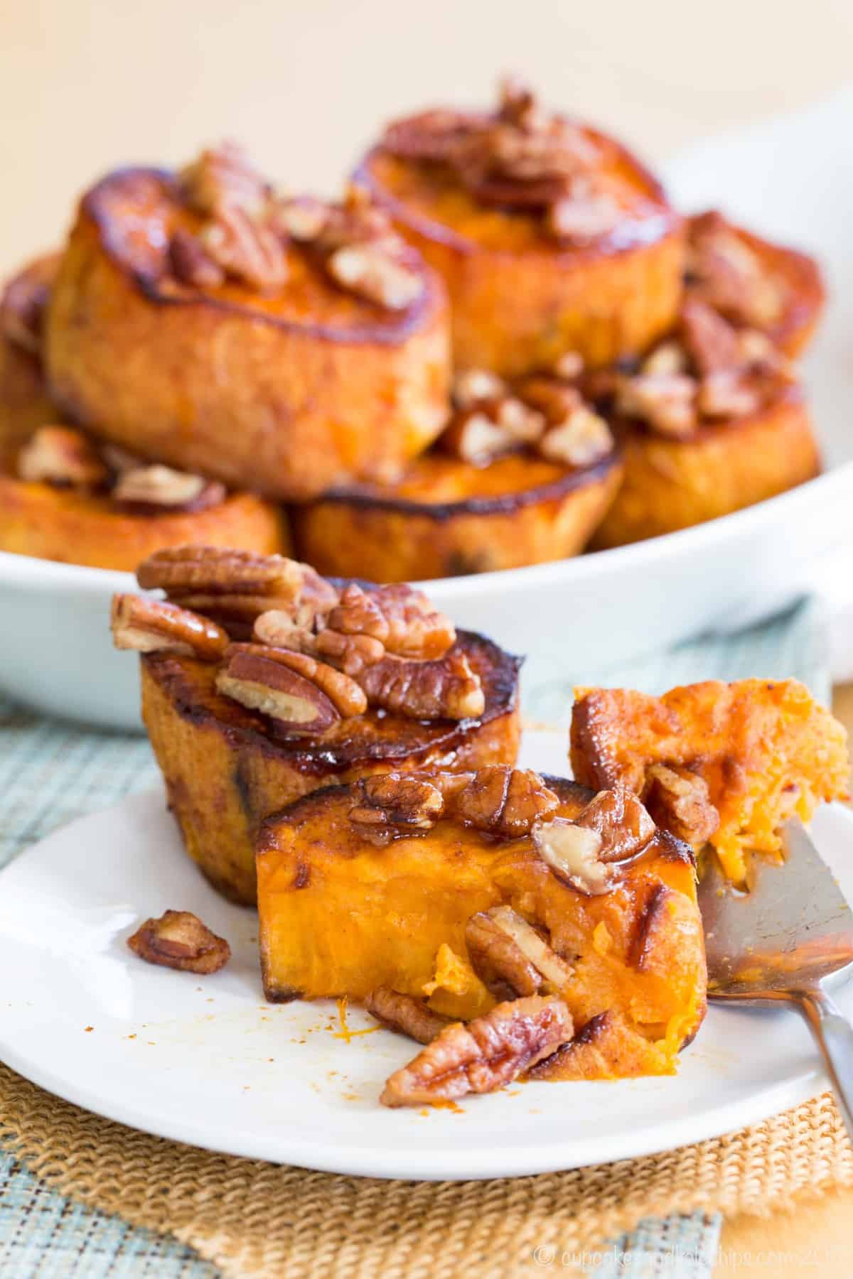 Maple glazed pecans on top of roasted sweet potatoes, cut open to reveal caramelized centers.