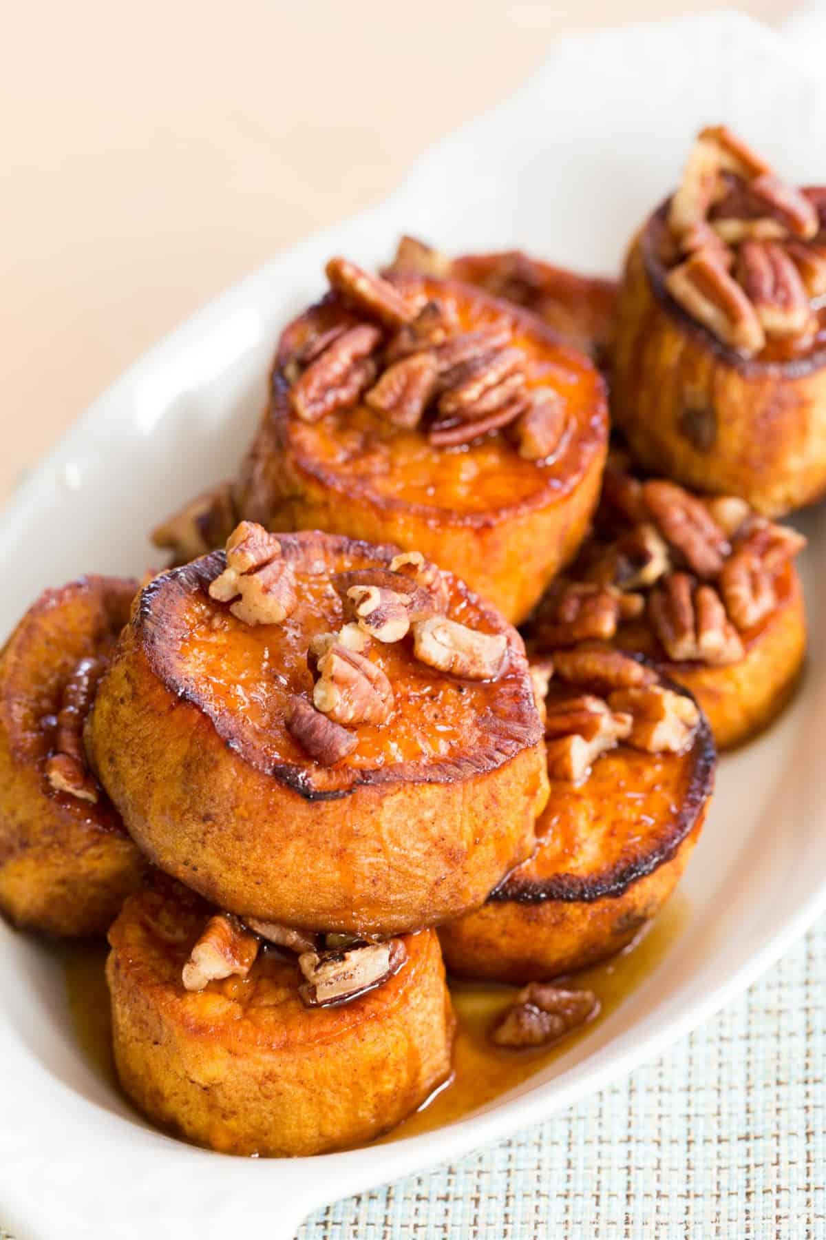 pecan-topped melting sweet potatoes in a white oval dish on a plaid cloth napkin