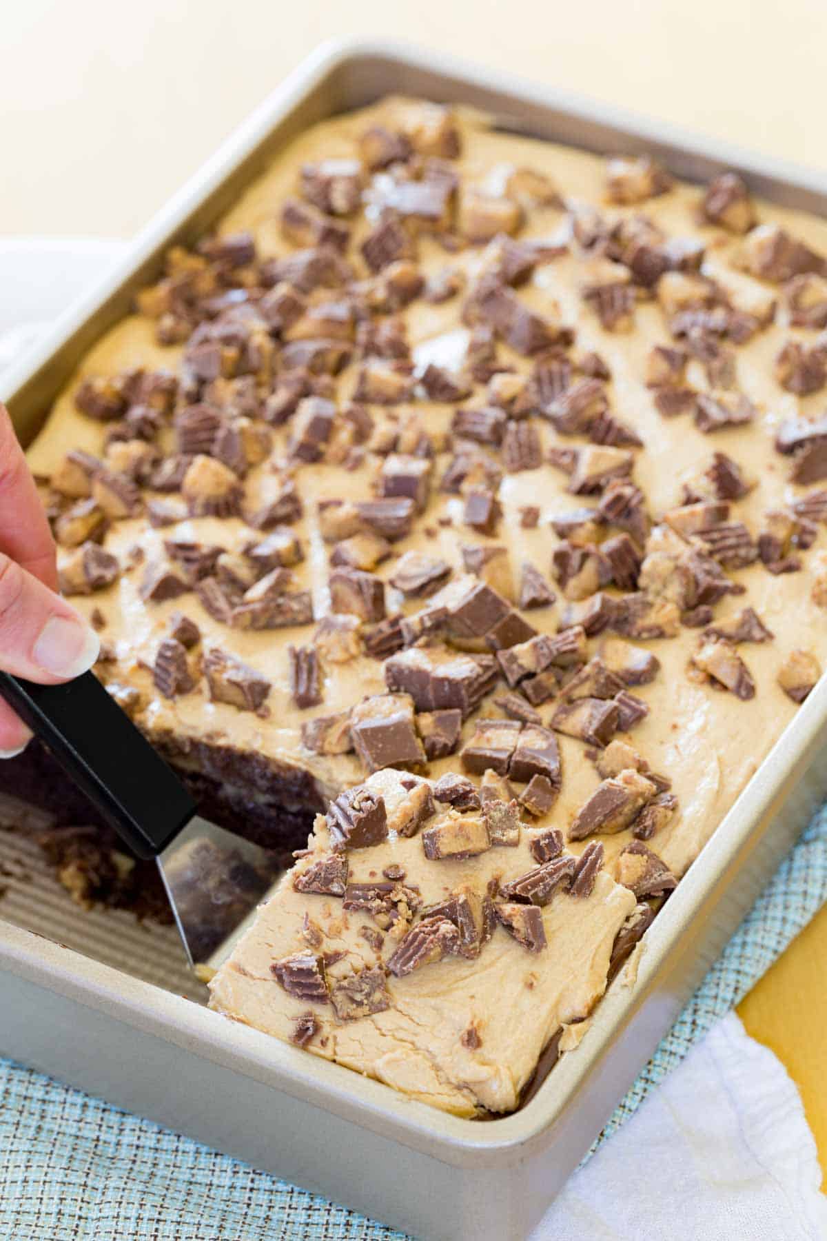 Reese's poke cake in a baking pan with one slice being picked up on a spatula.