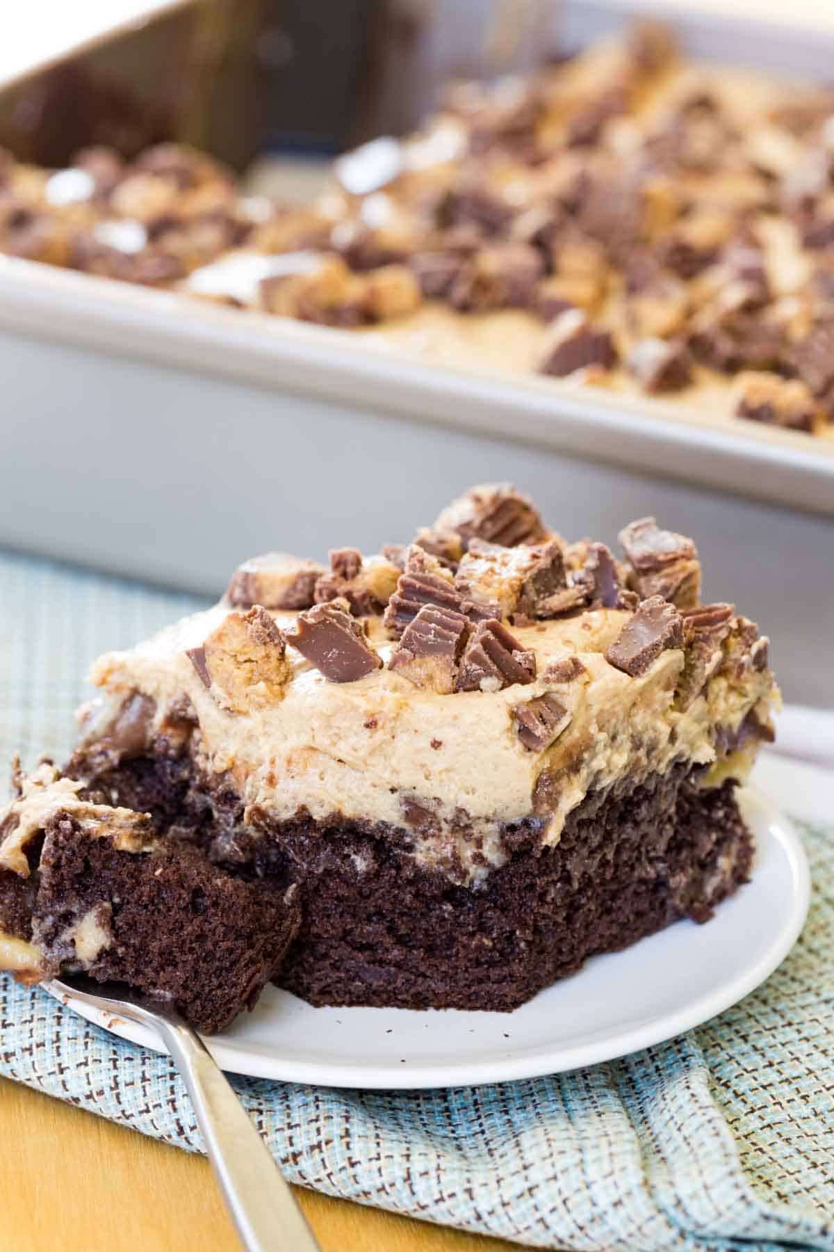 A piece of Reese's Poke Cake on a plate on top of a blue plaid cloth napkin.