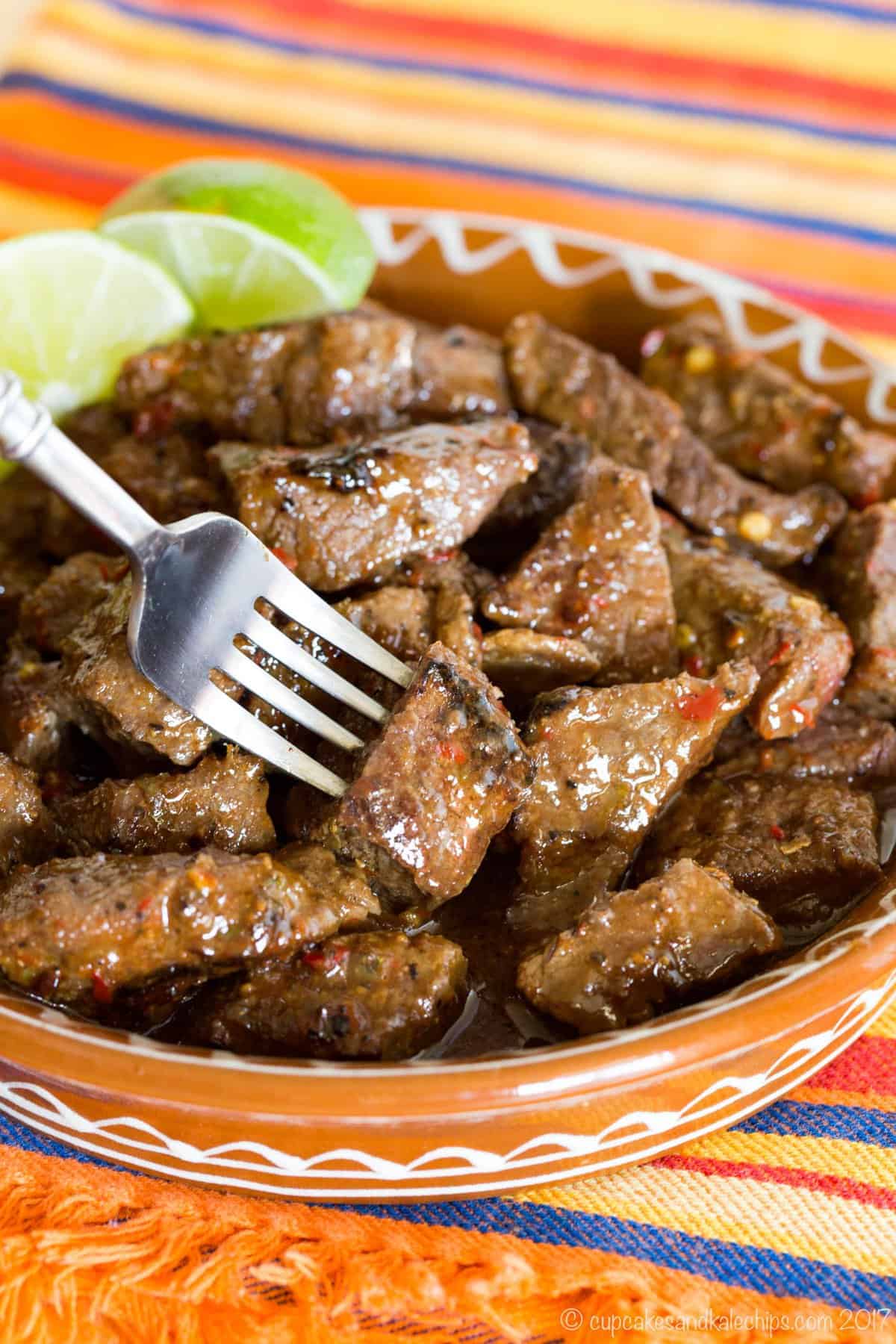 Chili Lime Steak Bites in a terra cotta dish with a fork stuck in one.