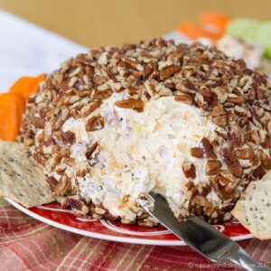 A cheese ball with some of it already removed to see the ham and cheese spread under the pecan coating.