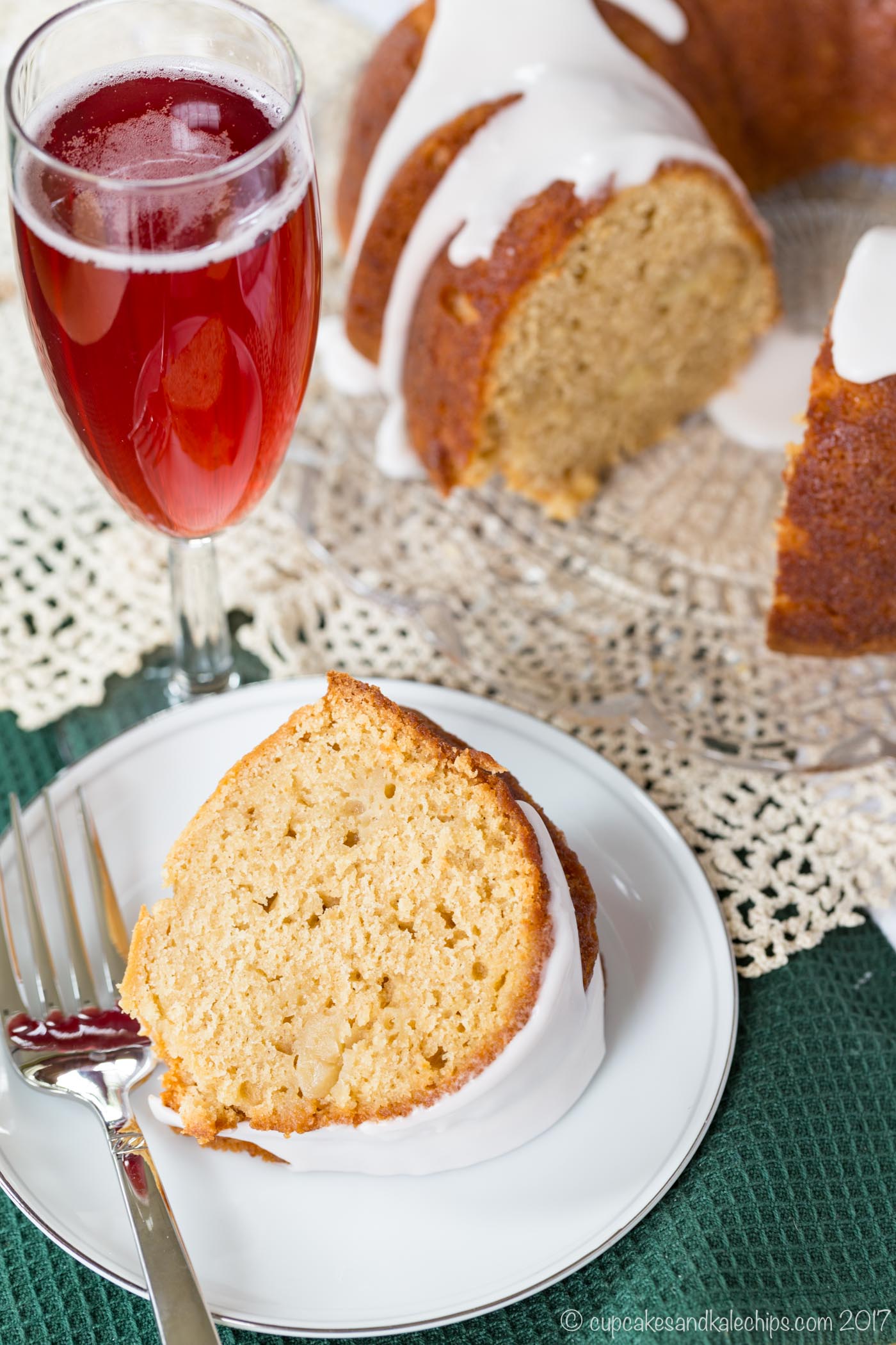 A slice of gluten-free apple cranberry donut cake on a plate next to a fork and a flute glass of Martinelli's sparkling cider.