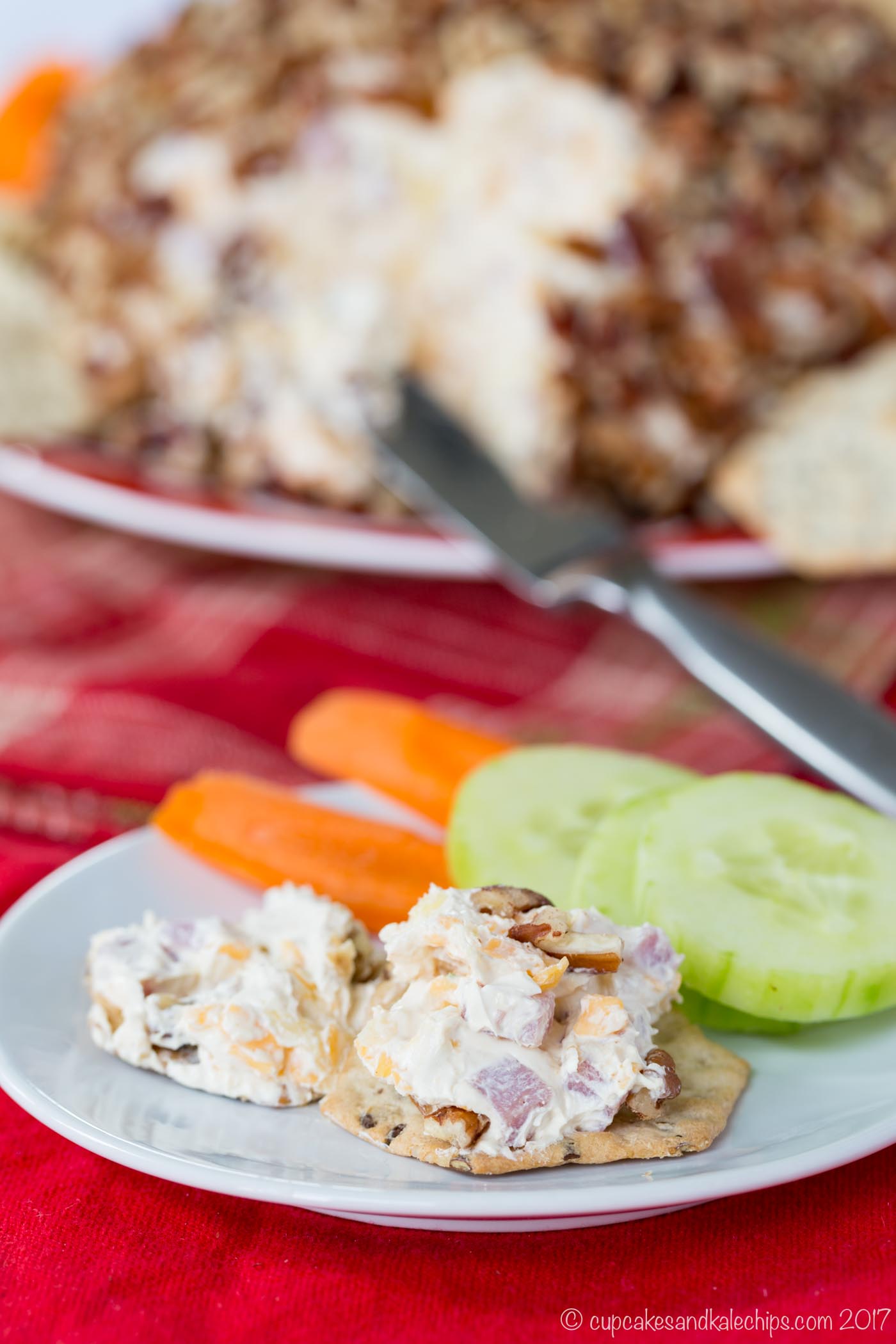 Ham and cheese spread on two crackers on a plate with some cucumber and carrot slices.