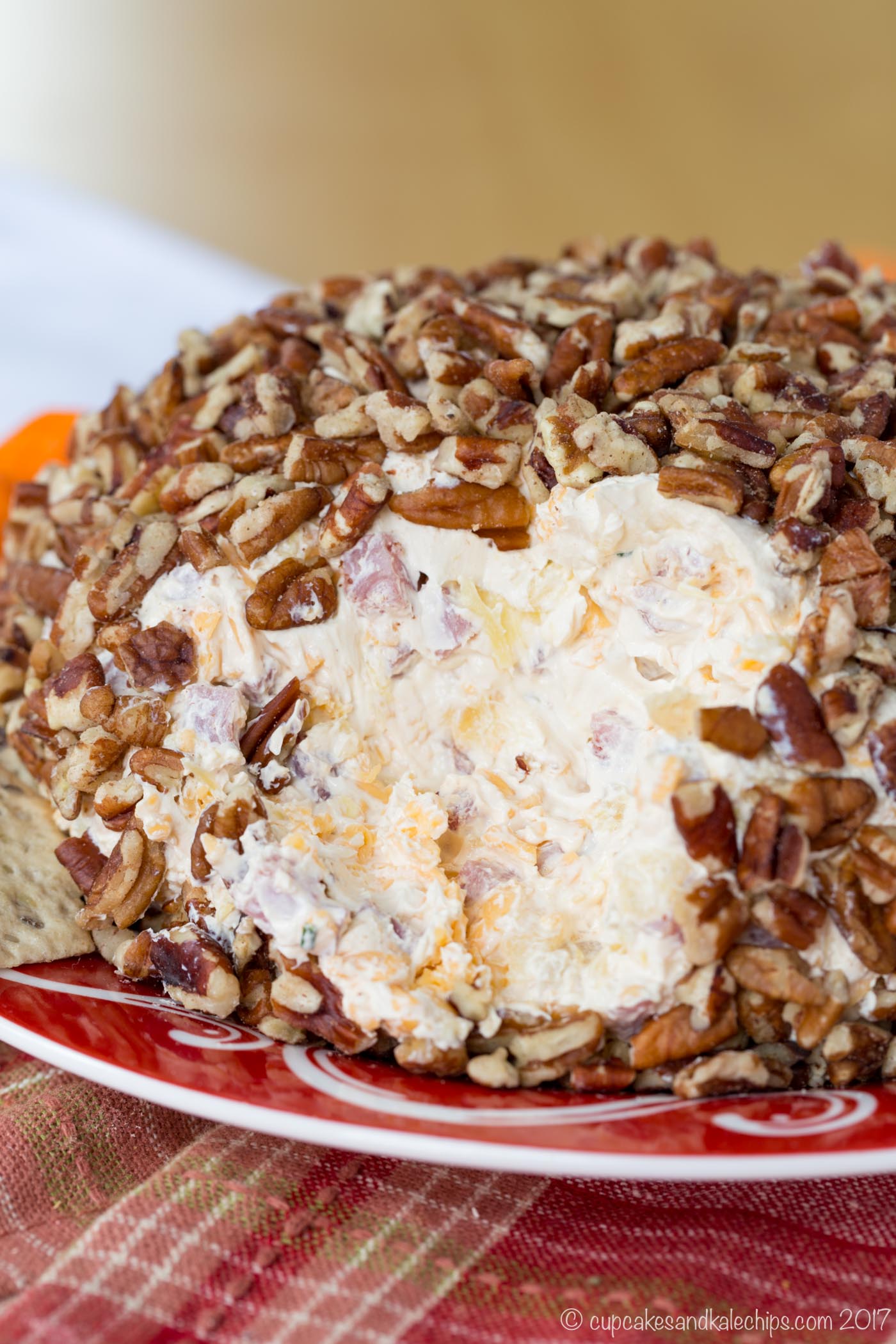 Closeup of the creamy ham and cheese spread in the interior of a pecan-coated cheeseball on a red and white plate.