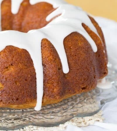 Gluten-free cranberry apple bundt cake on a cake stand with white icing dripping over the sides.