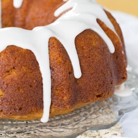 Gluten-free cranberry apple bundt cake on a cake stand with white icing dripping over the sides.