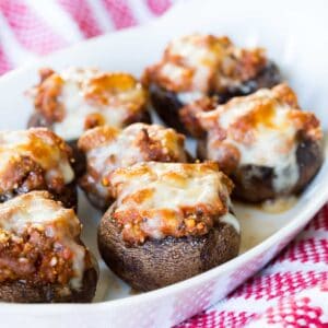 A white serving dish of Italian stuffed mushrooms topped with melted mozzarella cheese.
