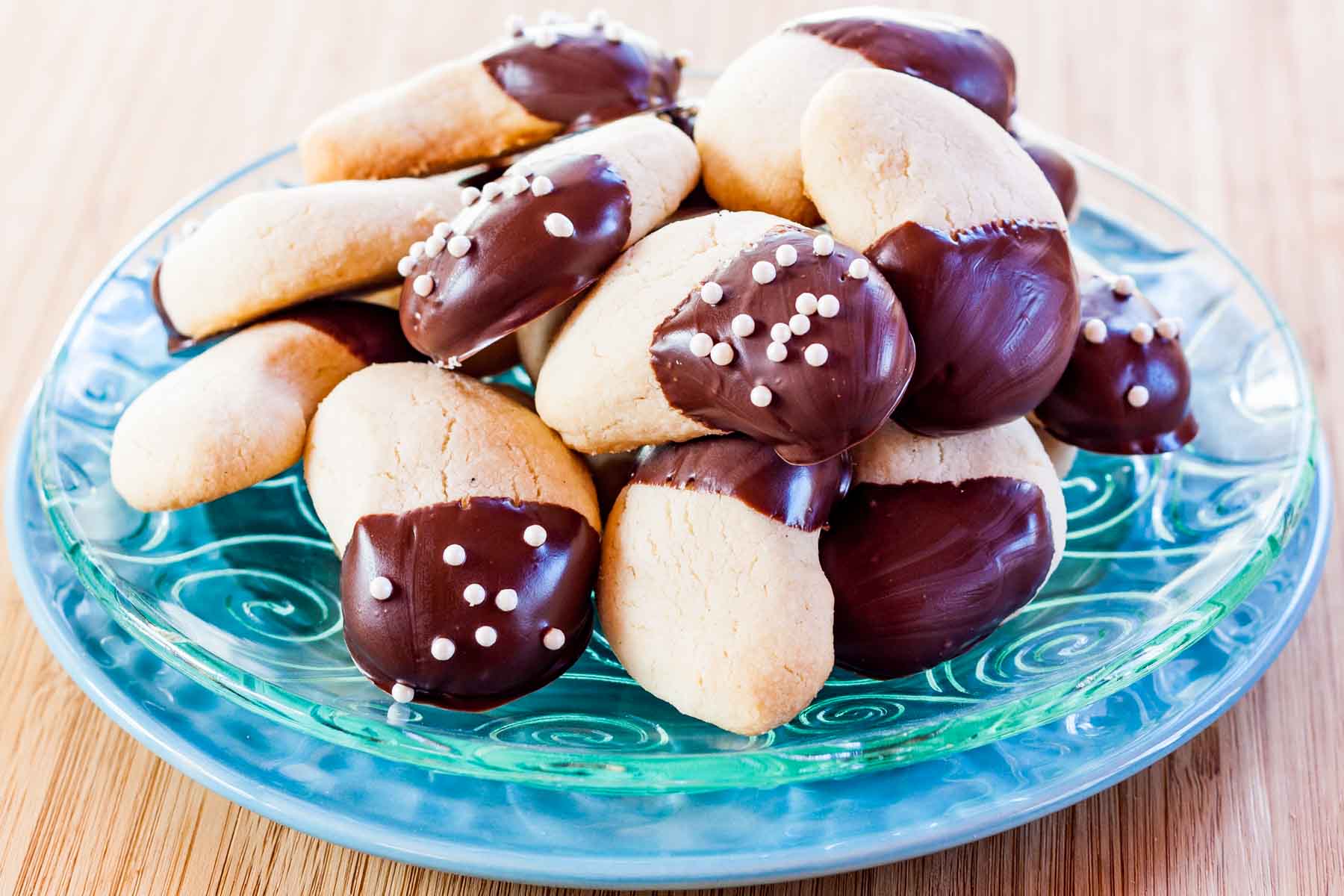 A pile of chocolate-dipped almond crescent cookies on a glass plate on top of a light blue plate.