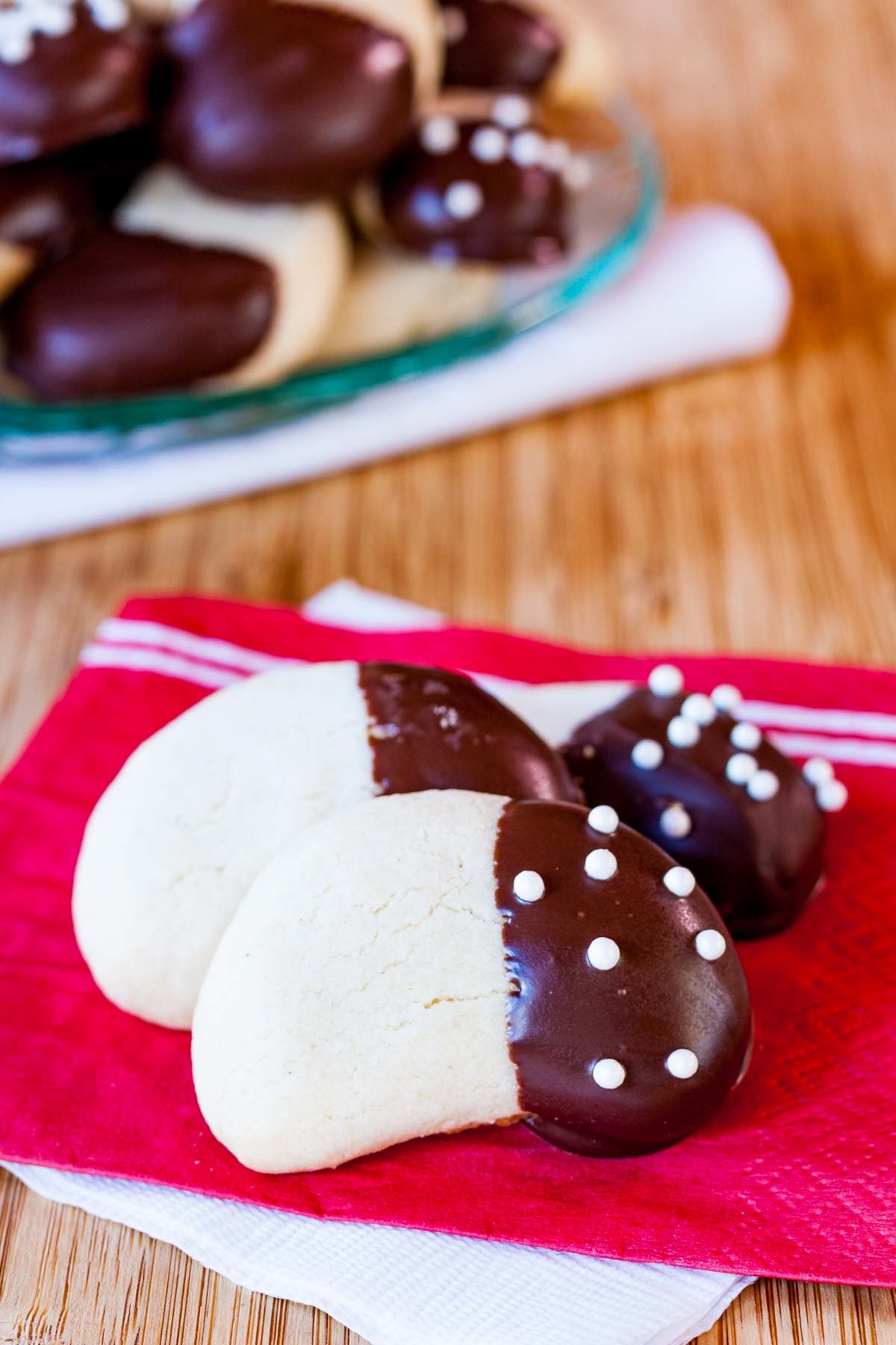 Three Almond crescent cookies with one end covered in dark chocolate and sprinkles on a couple of red and white napkins.