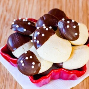 Gluten Free Almond Crescents dipped in chocolate overflowing from a red snowflake-shaped dish on a white mapkin.